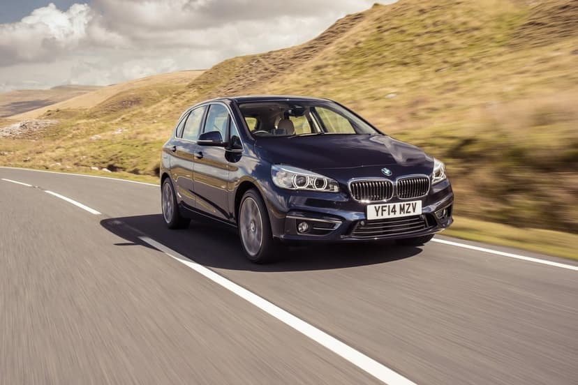 Dark blue BMW 2 Series Active Tourer driving on a winding road through rolling green and brown hills.