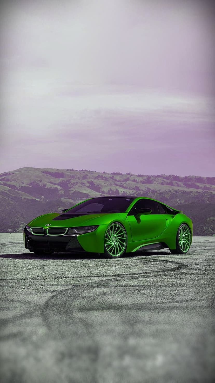 Lime green BMW i8 drifting on a mountain road with tire marks on asphalt against a purple mountain backdrop.