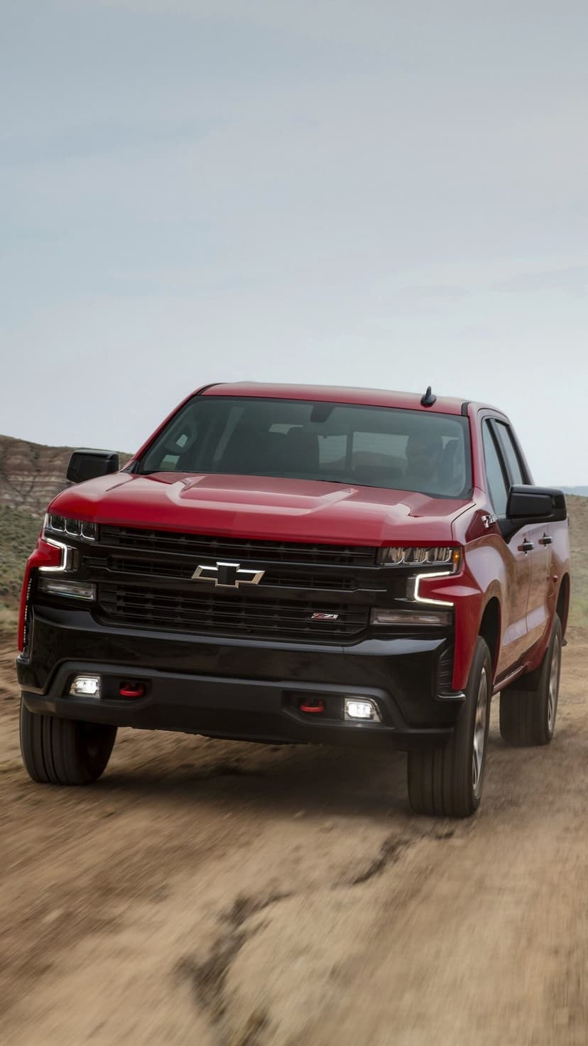 Red Chevrolet Silverado Z71 driving on a dusty dirt road with a black grille and glowing LED headlights.