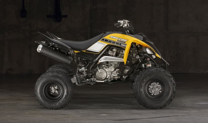 Profile of a yellow and black Yamaha Raptor 700R ATV against a dark concrete wall with studio lighting.