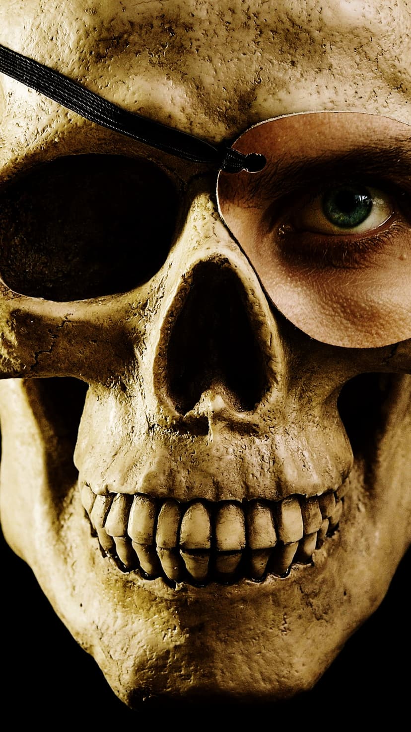 Weathered skull wearing a black leather eye patch with a single piercing green human eye staring from the socket.