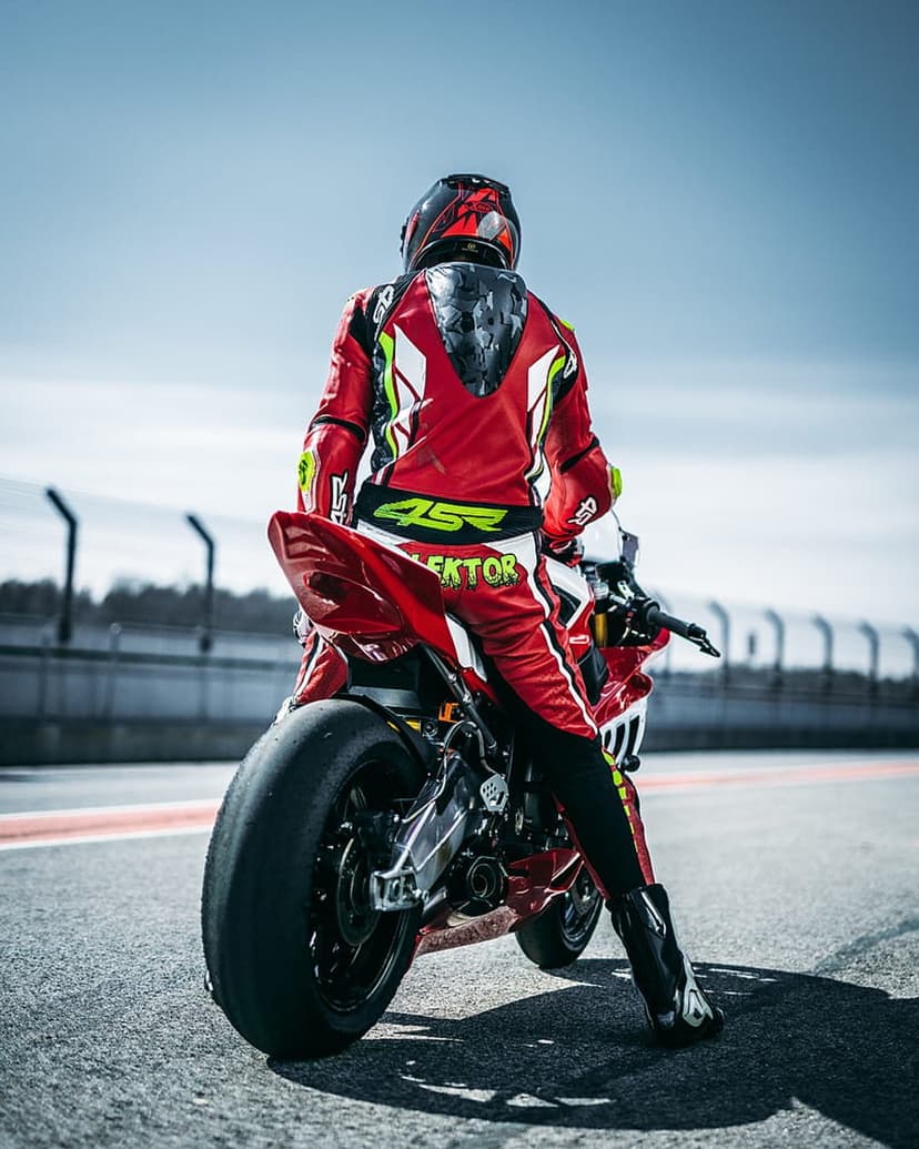 Motorcycle racer in a red and white suit leans on a sportbike during a race under a clear blue sky.