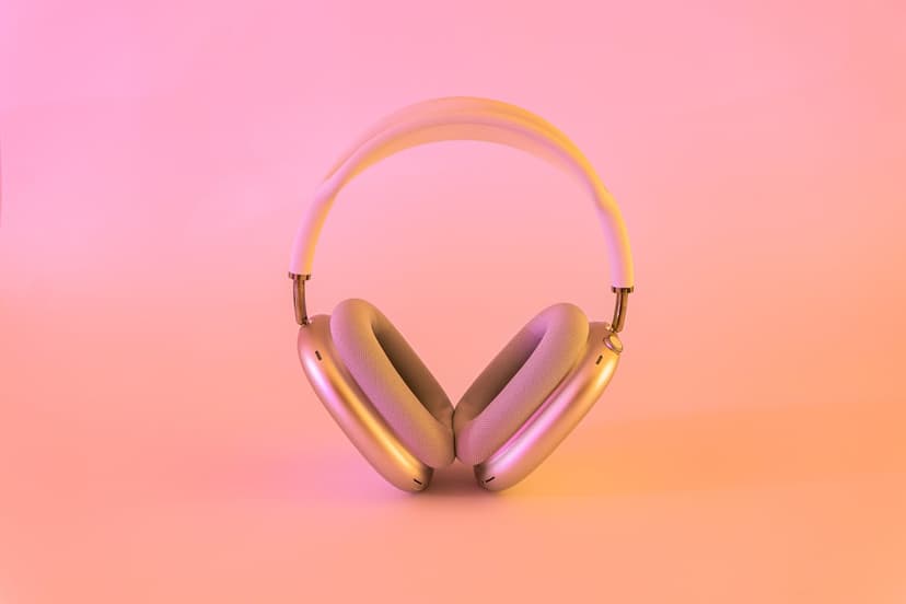 Silver metallic headphones positioned vertically against a soft pink and orange gradient with warm reflections.