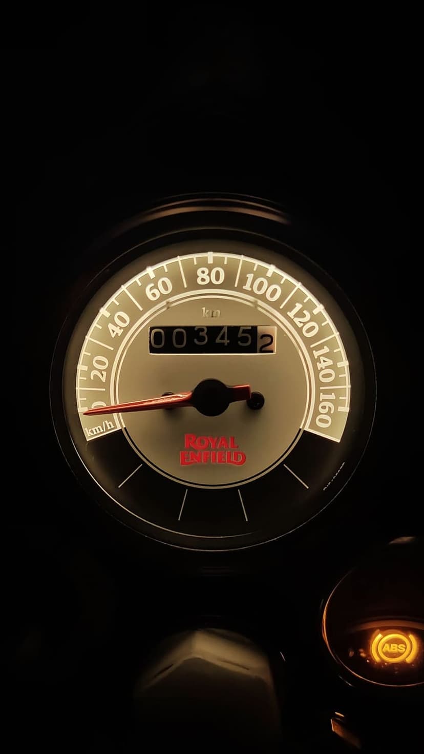 Royal Enfield speedometer glowing in the dark with an orange ABS light and analog needle on a motorcycle dash.