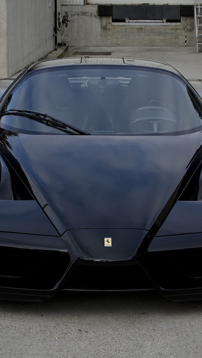 Black Ferrari Enzo with a reflective hood and the prancing horse emblem positioned on a vertical mobile screen.