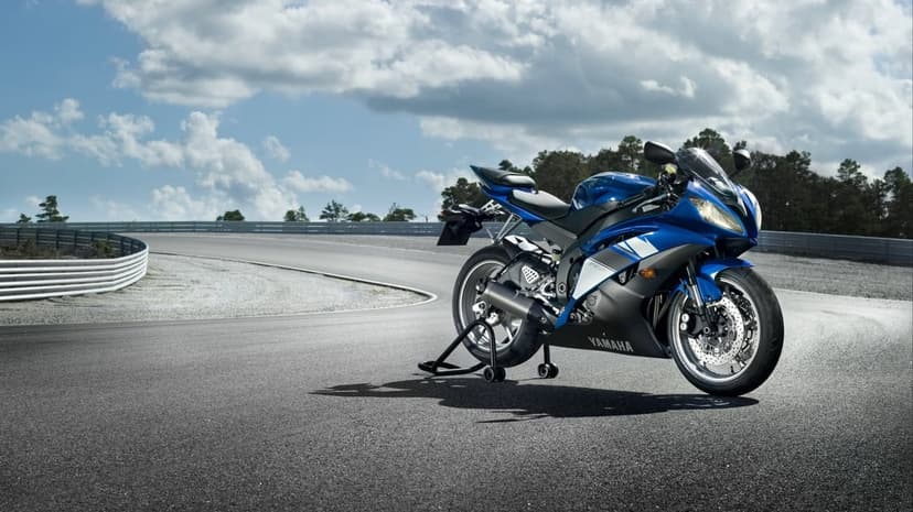 Blue Yamaha sport motorcycle on a paddock stand atop a curved asphalt race track under a bright cloudy sky.