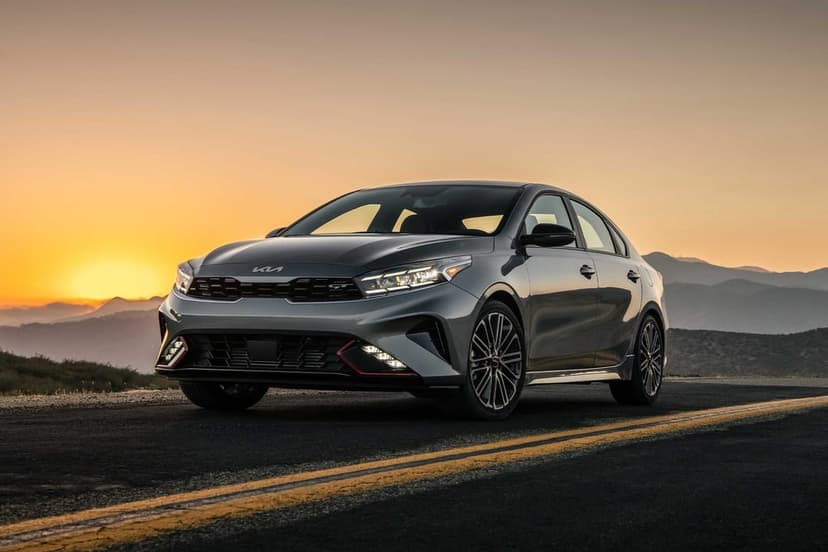Gray Kia Forte GT sedan on an open road against a golden sunset and mountain silhouettes.