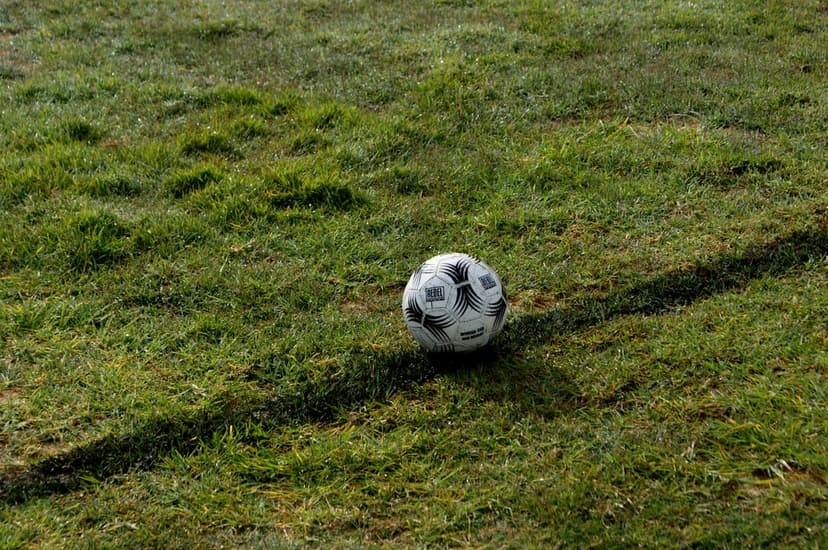 Soccer ball with black and white panels casting a long shadow over a bright green lawn under direct sunlight.