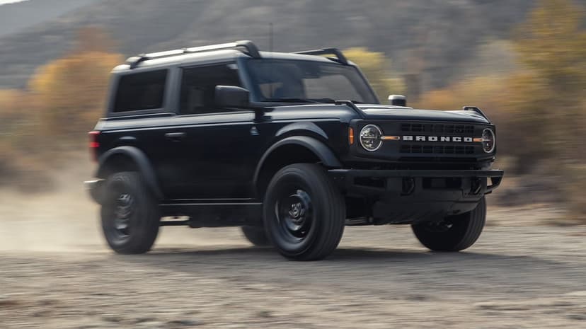 Black 2-door Ford Bronco driving fast on a dirt trail with motion blur and rising dust clouds.
