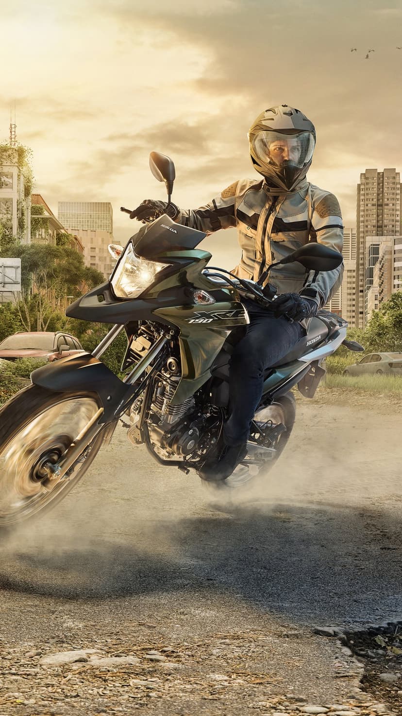 Motorcyclist in full gear kicks up dust while navigating a debris-filled street among overgrown city ruins.
