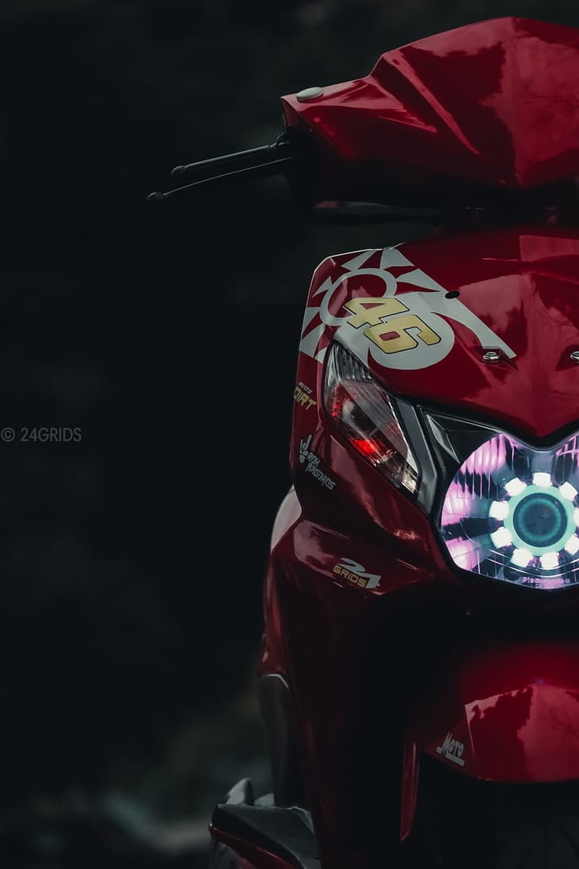 Red scooter front fairing with a number 46 decal and a glowing circular LED headlight on a dark background.