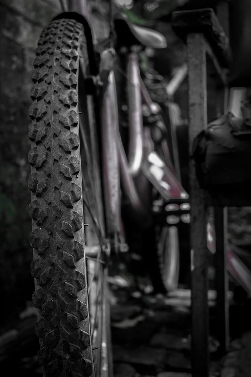 Mountain bike tire with deep tread patterns appears in sharp focus against a blurred frame and handlebar background.