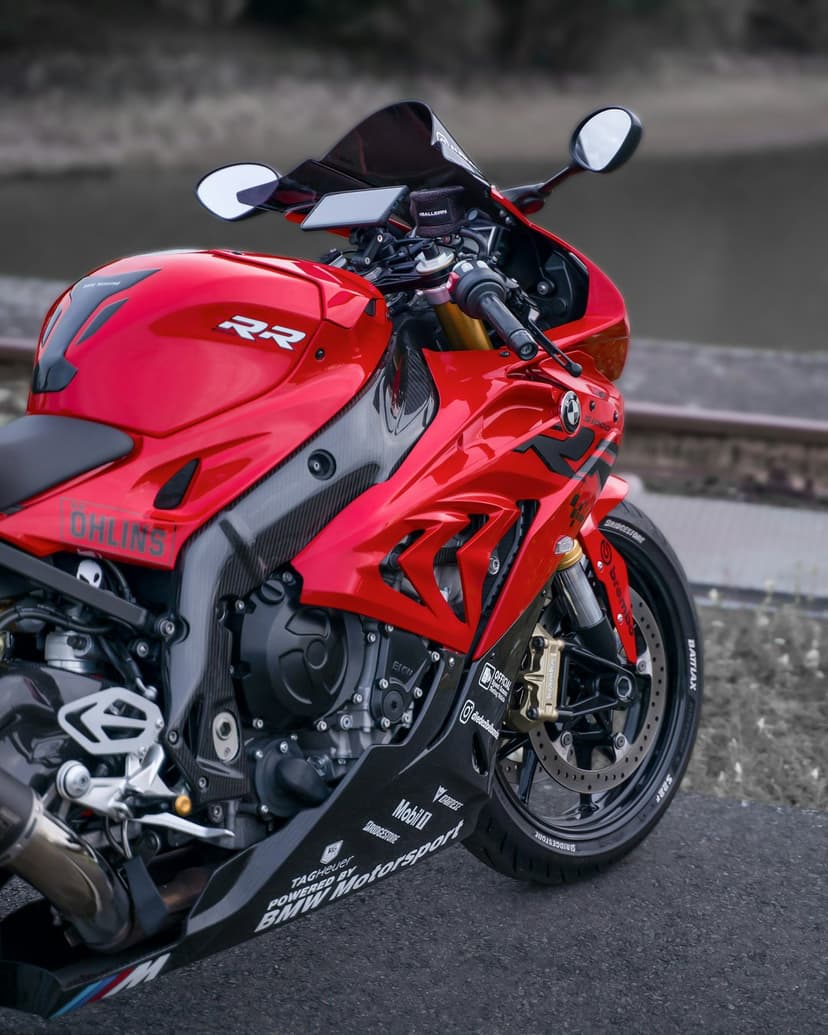 Red BMW S1000RR sportbike with racing decals parked on asphalt next to weathered steel railroad tracks.