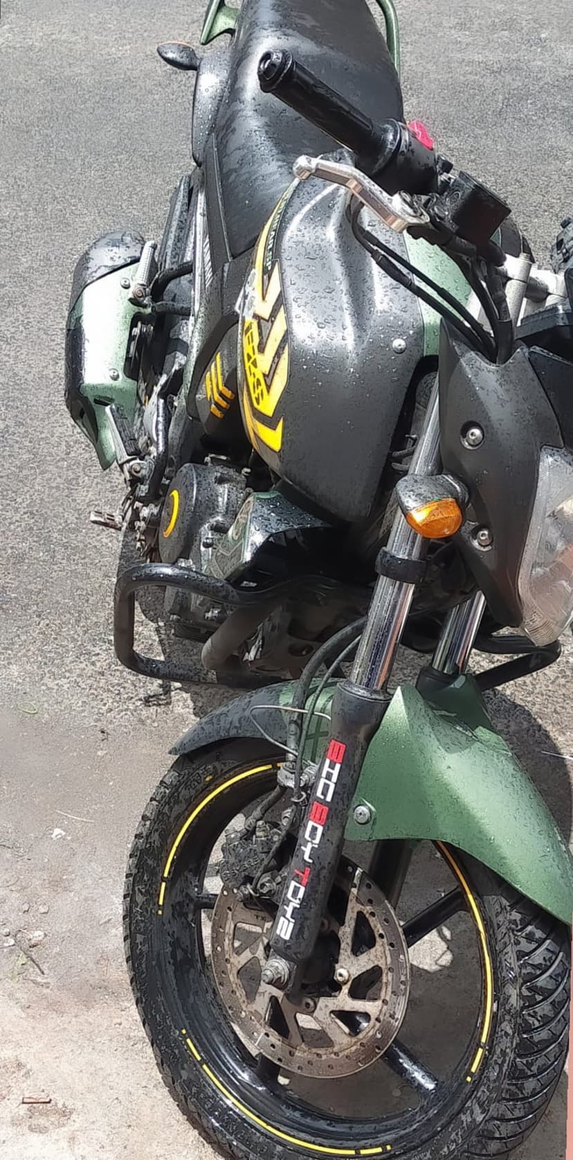 Green motorcycle with yellow stripes and water droplets on the fuel tank, featuring a front disc brake and tire.