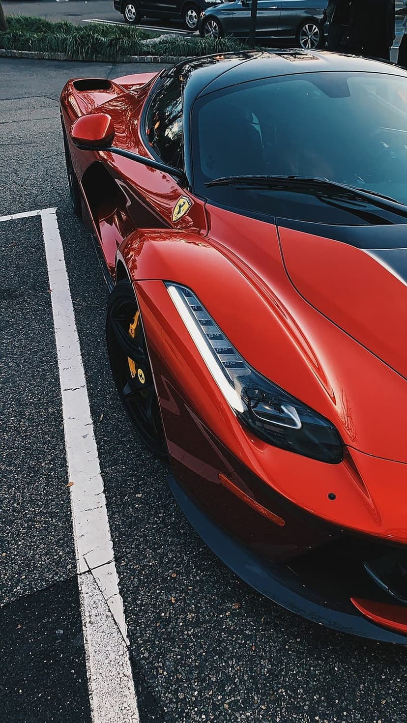 Red Ferrari sports car front grille and logo on asphalt, highlighting sleek curves and metallic paint texture.