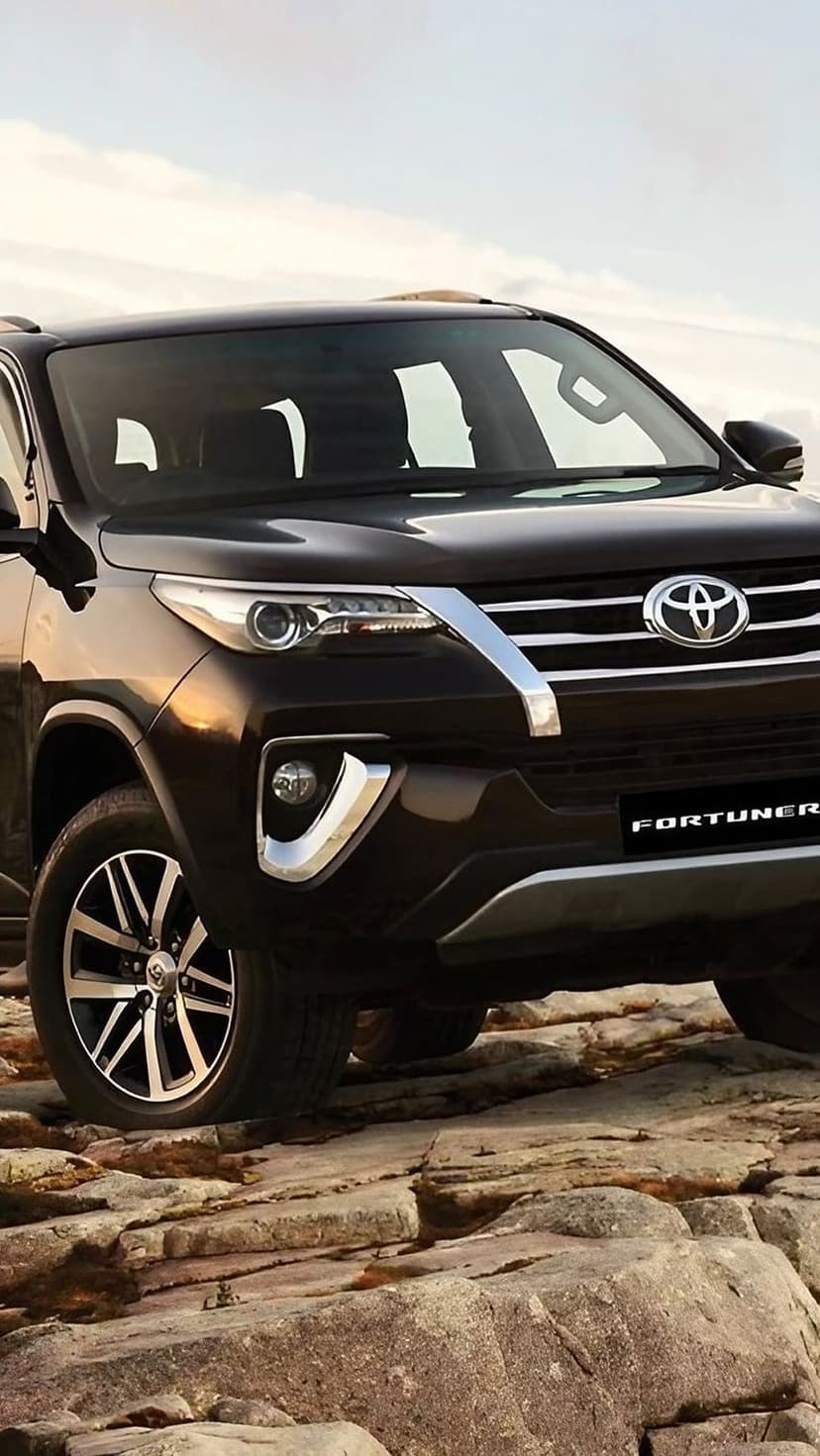 Toyota Fortuner SUV parked on sharp mountain rocks showing its alloy wheels and chrome grille under a bright sky.