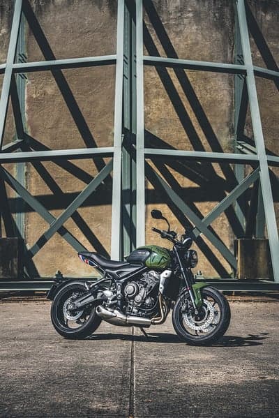 Green Triumph Motorcycle Parked Against Industrial Structure