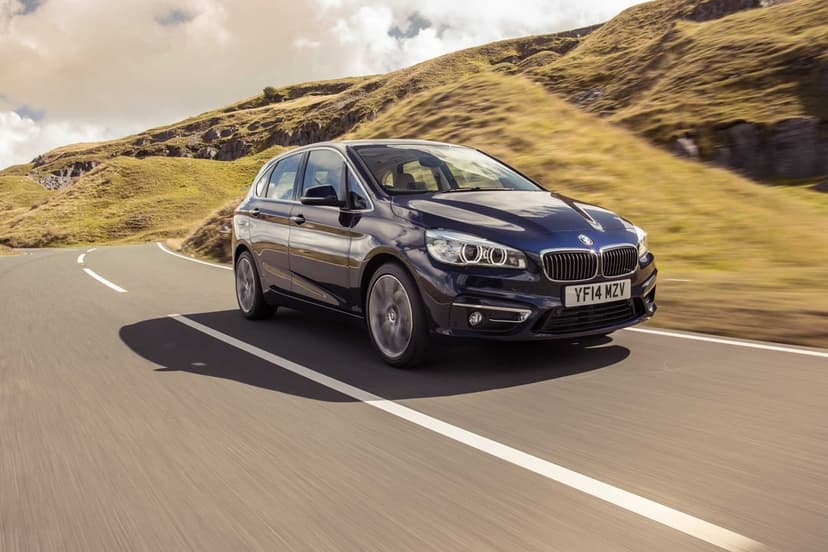 Dark blue BMW 2 Series Active Tourer driving on a winding asphalt road through green rolling hills.