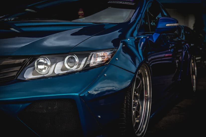 Metallic blue sports car with flared widebody fenders and glowing circular LED headlights in a low-angle shot.