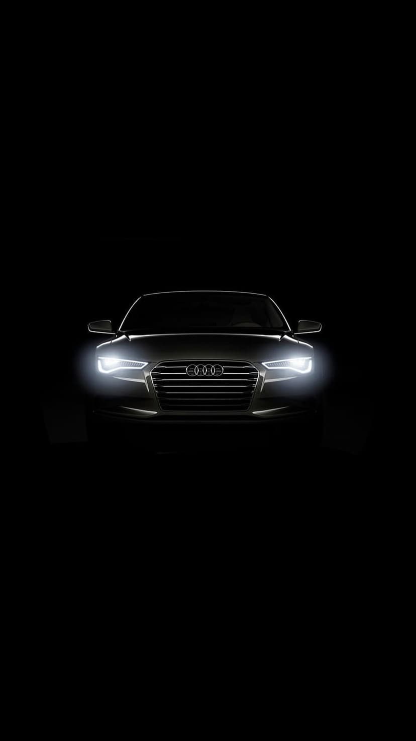 Audi front grille with glowing white LED headlights and chrome emblem centered against a pitch-black background.