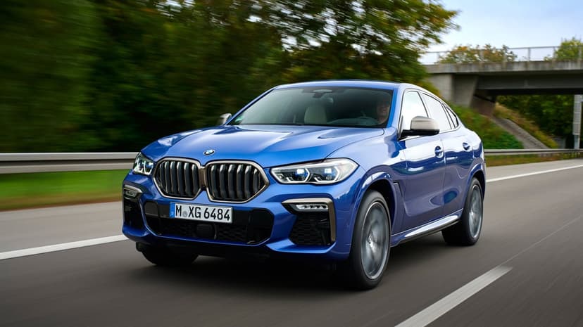 Blue BMW X6 M50i luxury SUV driving on a highway with motion blurred trees and a bridge in the background.
