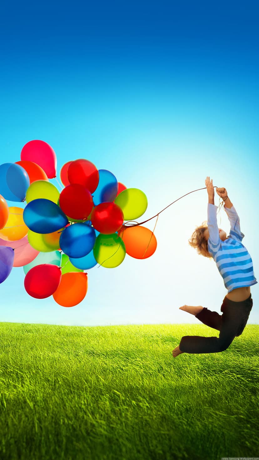 Young child jumps high in a grassy meadow while holding colorful balloons under a clear, bright blue sky.