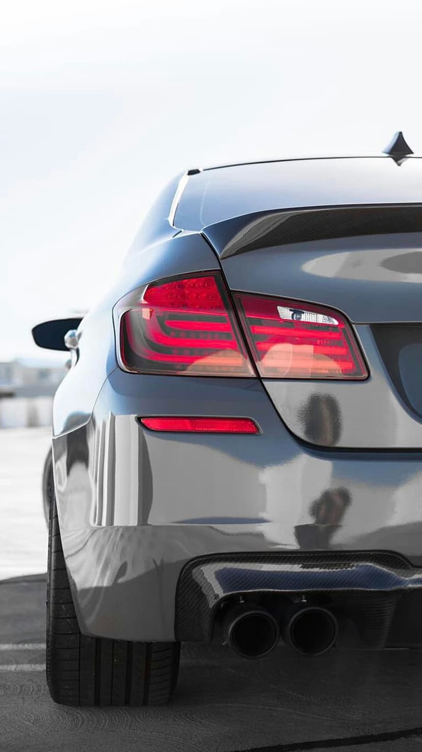 Gray luxury sedan rear view showing red LED taillights, a carbon fiber diffuser, and dual chrome exhaust pipes.