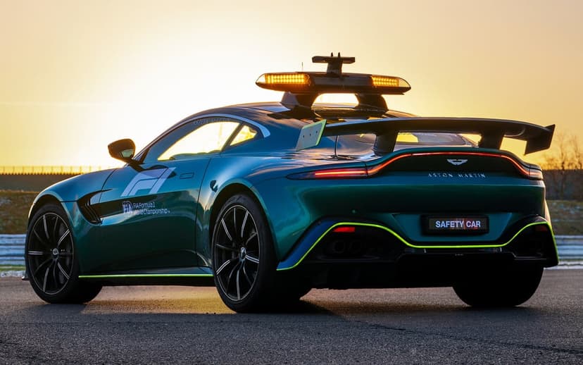 Aston Martin F1 Safety Car in British Racing Green with lit amber lights at sunset on a racetrack.