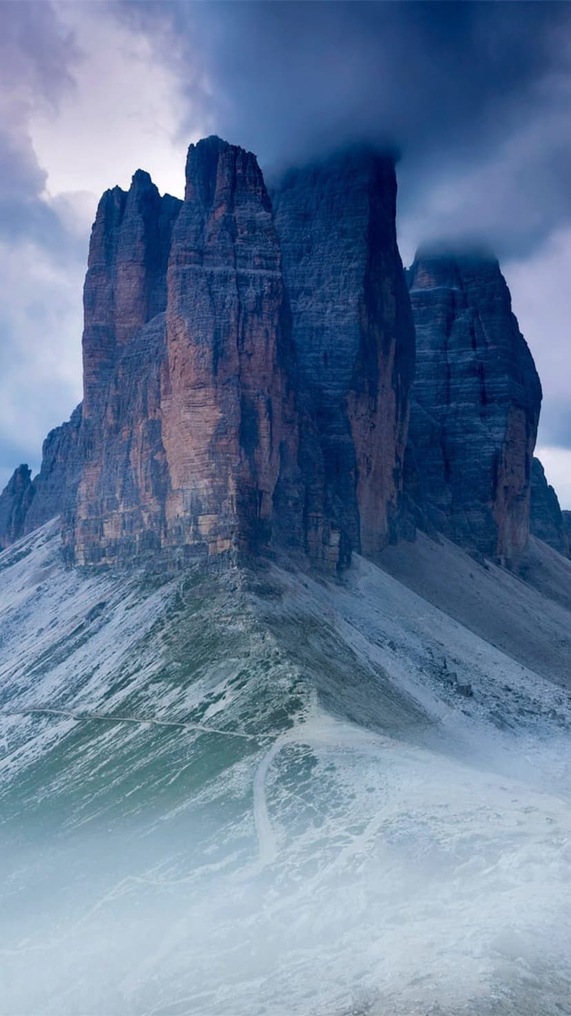 Tre Cime di Lavaredo peaks stand tall amidst thick mountain mist and dark storm clouds with frost on the slopes.