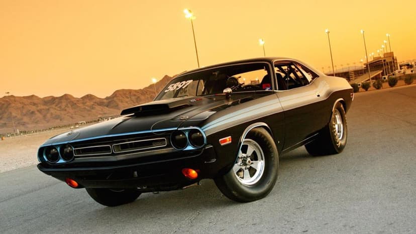 Black classic muscle car on a drag strip at sunset with a golden sky and desert mountains in the background.