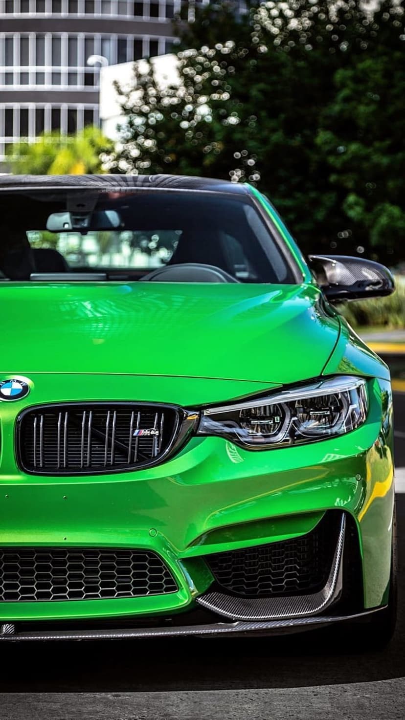 BMW M4 in metallic green features a signature kidney grille and sharp headlights under bright outdoor sunlight.