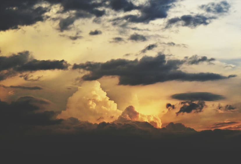 Towering cumulonimbus clouds illuminated by fiery orange sunset light against a dark charcoal sky background.