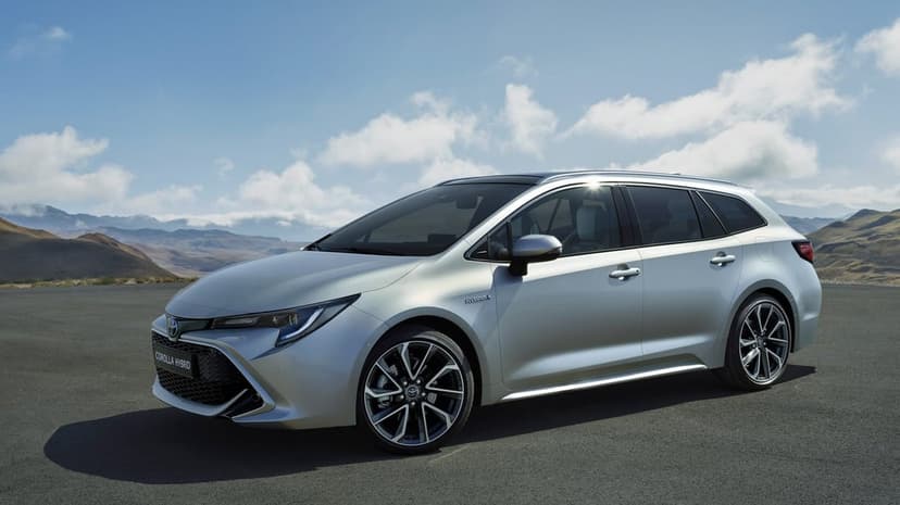 Silver Toyota Corolla Hybrid Touring Sports parked on asphalt with a scenic mountain and blue sky background.