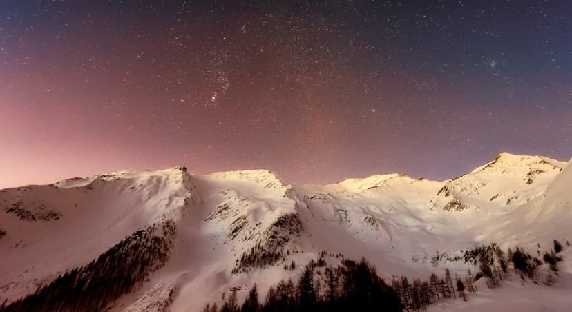 Snow-capped mountain peaks under a violet and blue starry night sky during a clear winter twilight transition.