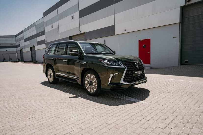 Dark green Lexus LX 570 luxury SUV parked on a paved lot in front of a grey and white industrial building.