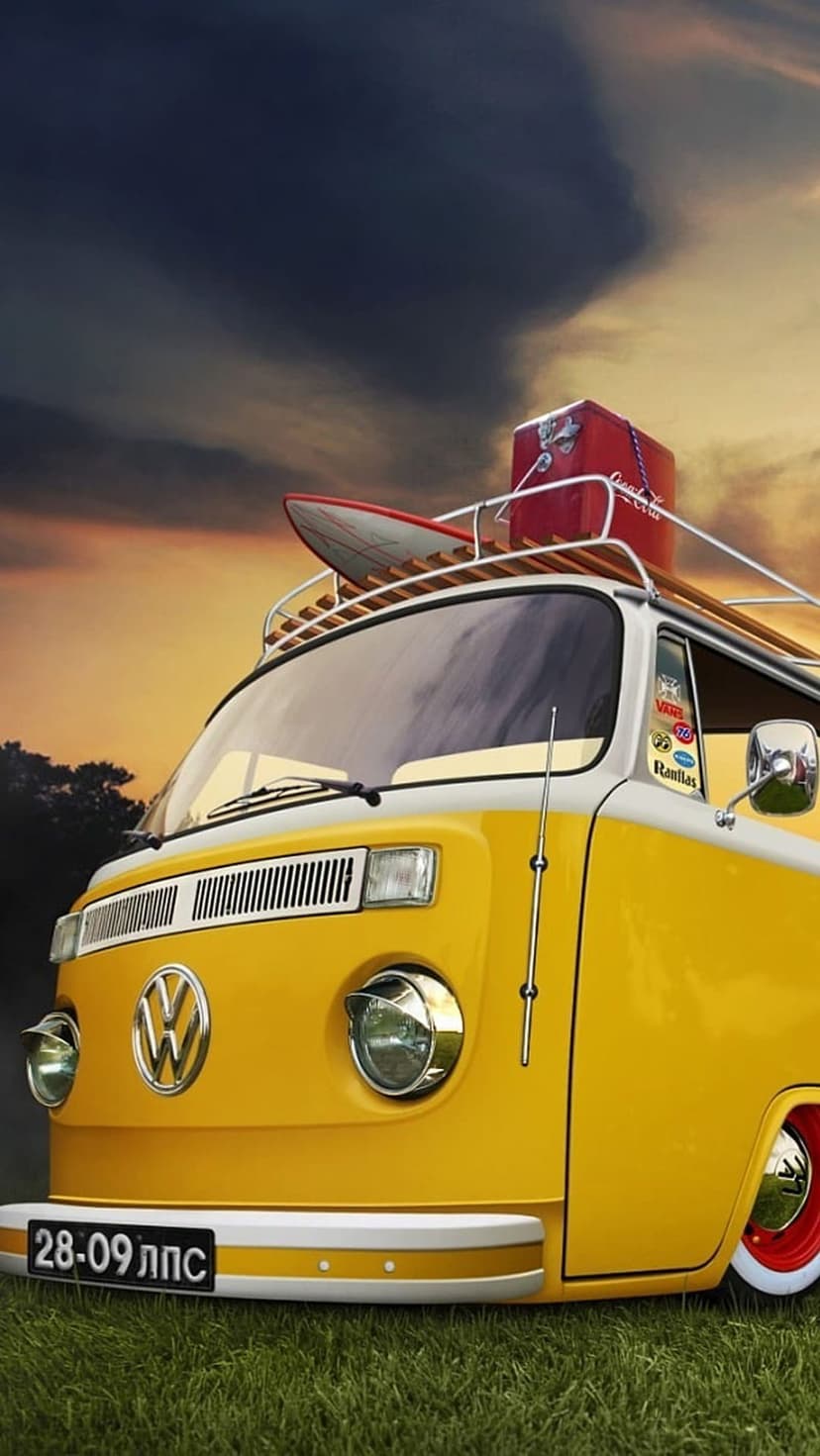 Yellow vintage Volkswagen van with a surfboard and red suitcase on its roof rack parked on a grassy field.