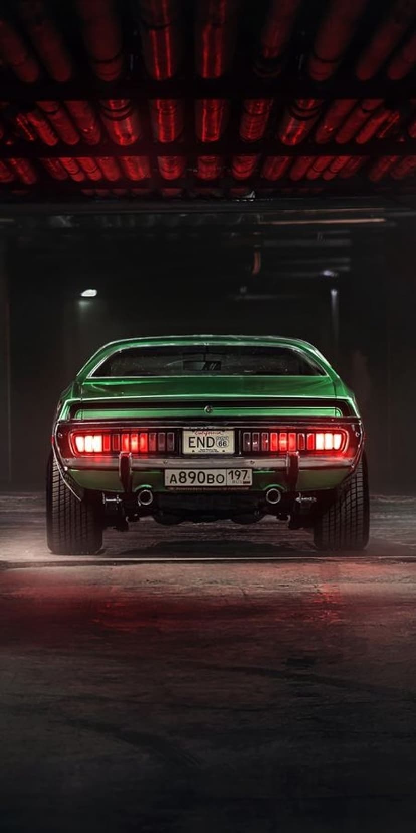 Green muscle car with glowing red taillights and chrome bumpers parked in a dimly lit industrial garage scene.