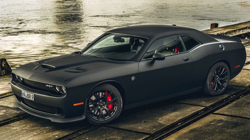 Matte black Dodge Challenger SRT Hellcat with red brake calipers on a concrete pier by the water.