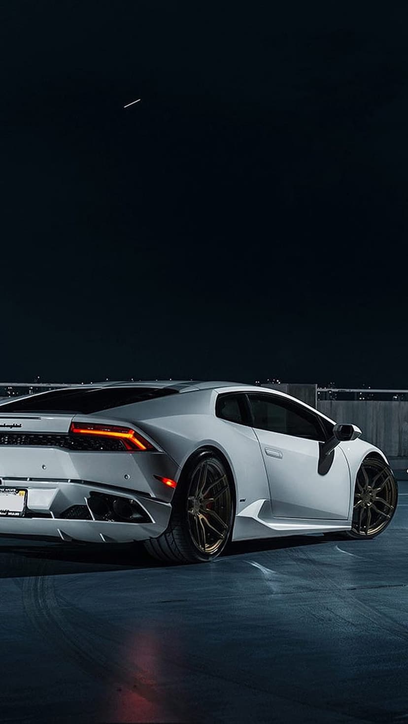 White Lamborghini Huracan rear view with glowing taillights and bronze wheels on dark asphalt at night.