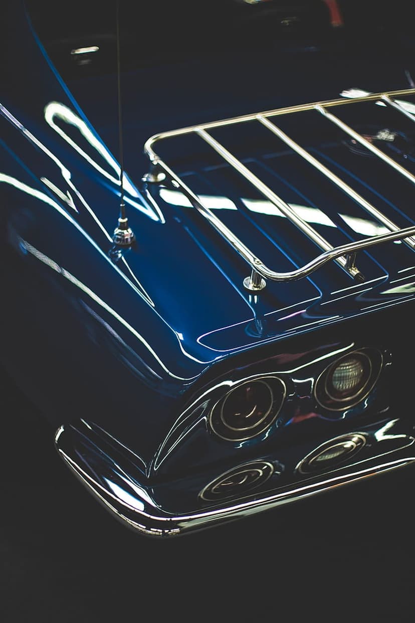Blue vintage car rear featuring a chrome luggage rack and round taillights against a dark, moody background.