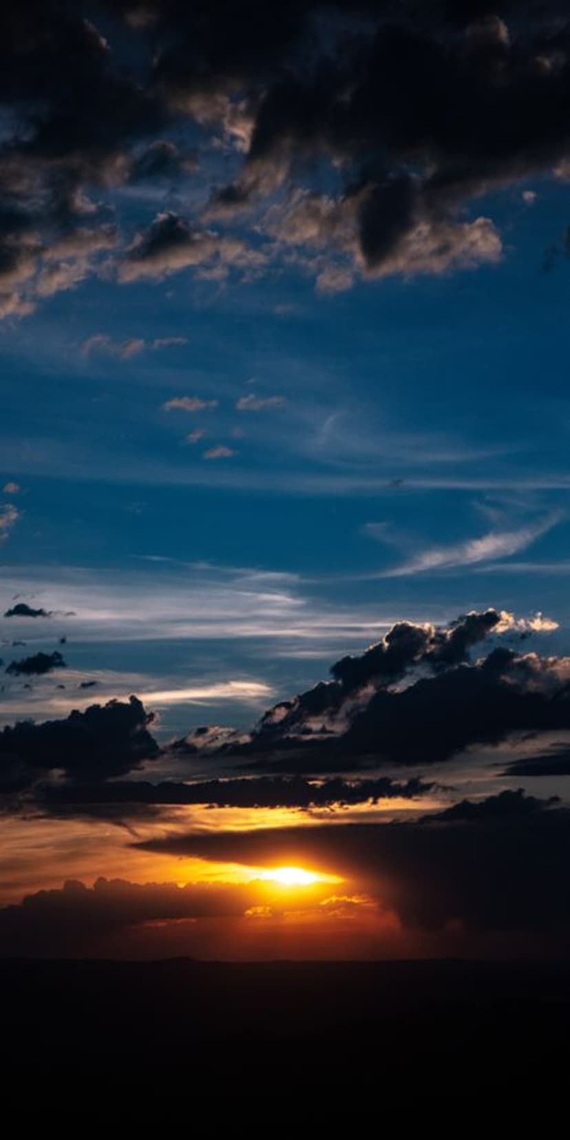 Vibrant orange and yellow clouds float in a twilight sky over a dark silhouette of a flat horizon line.