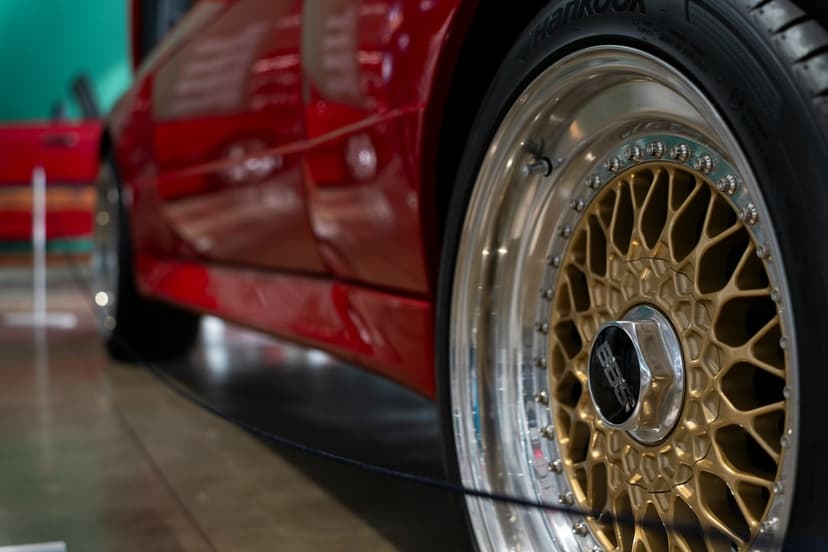Gold BBS mesh wheel on a red vintage car features polished chrome rims and glossy paint in a low-angle shot.
