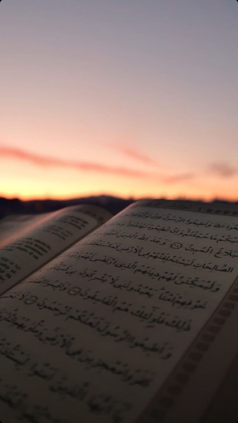 Open Quran with Arabic script glows under a pink and orange twilight sky during the golden hour at dusk.