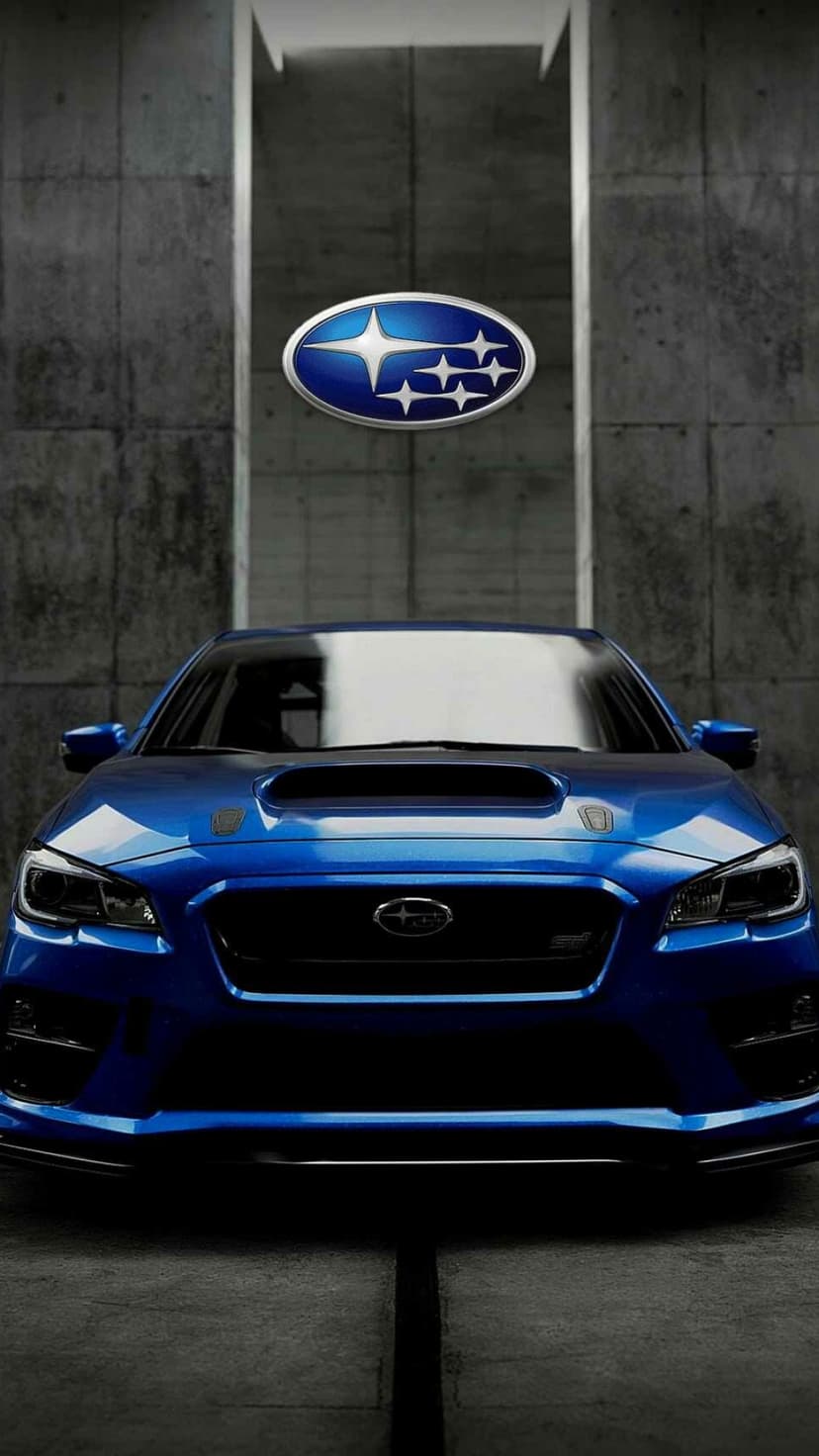 Blue Subaru WRX STI front view with an aggressive hood scoop and LED headlights against a textured concrete wall.