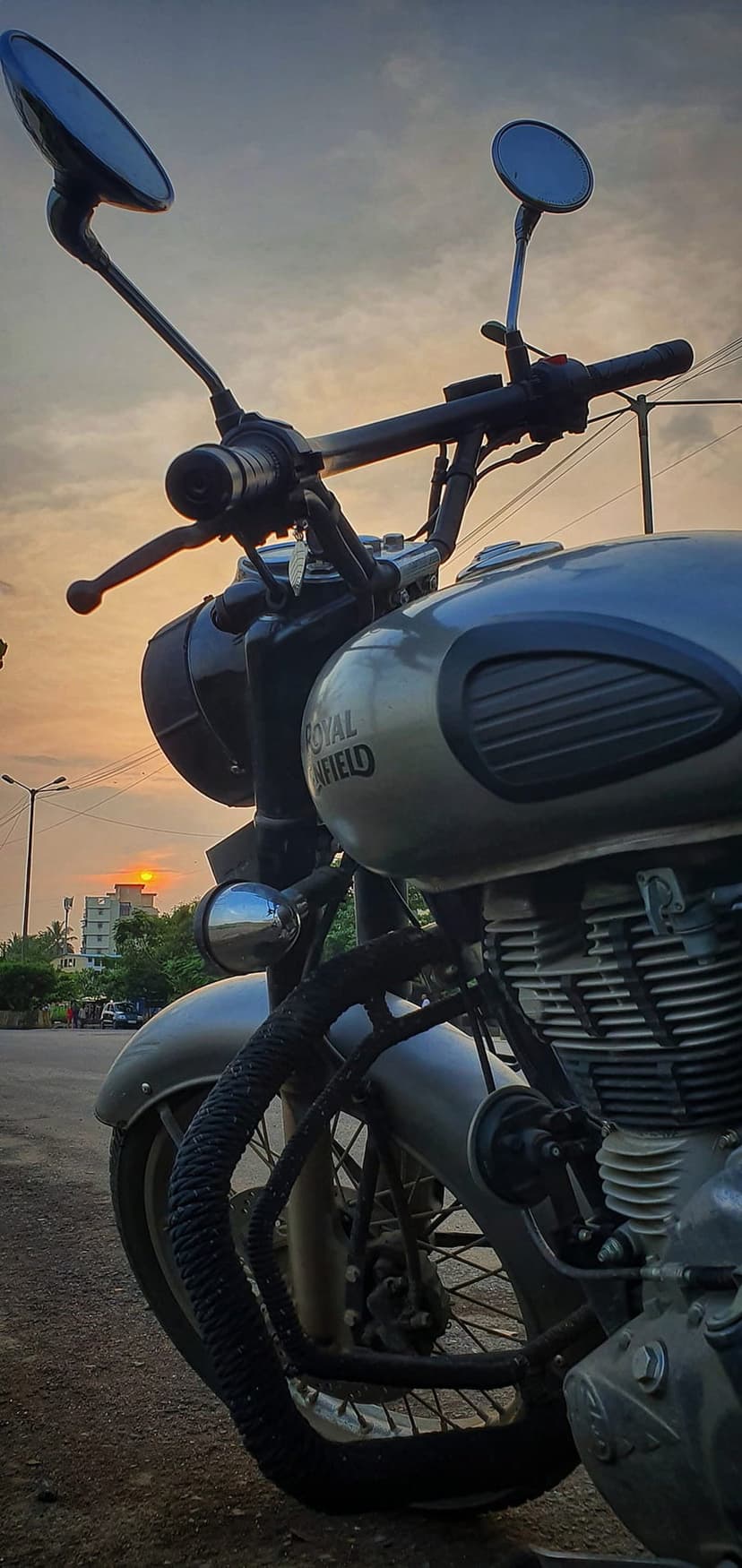 Silver Royal Enfield motorcycle engine and headlight reflecting warm orange light from a vibrant sunset sky.