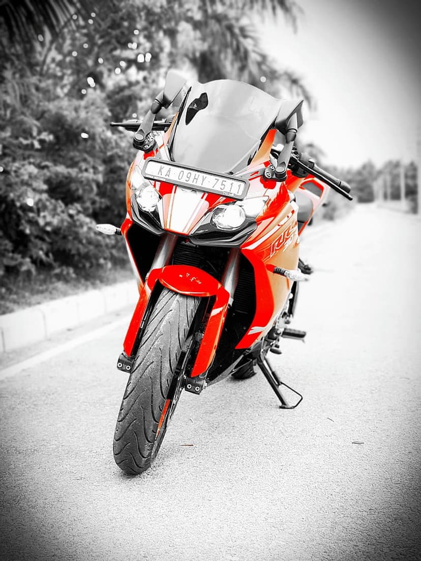 Red sports motorcycle parked on an asphalt road with a black and white forest background in sharp focus.
