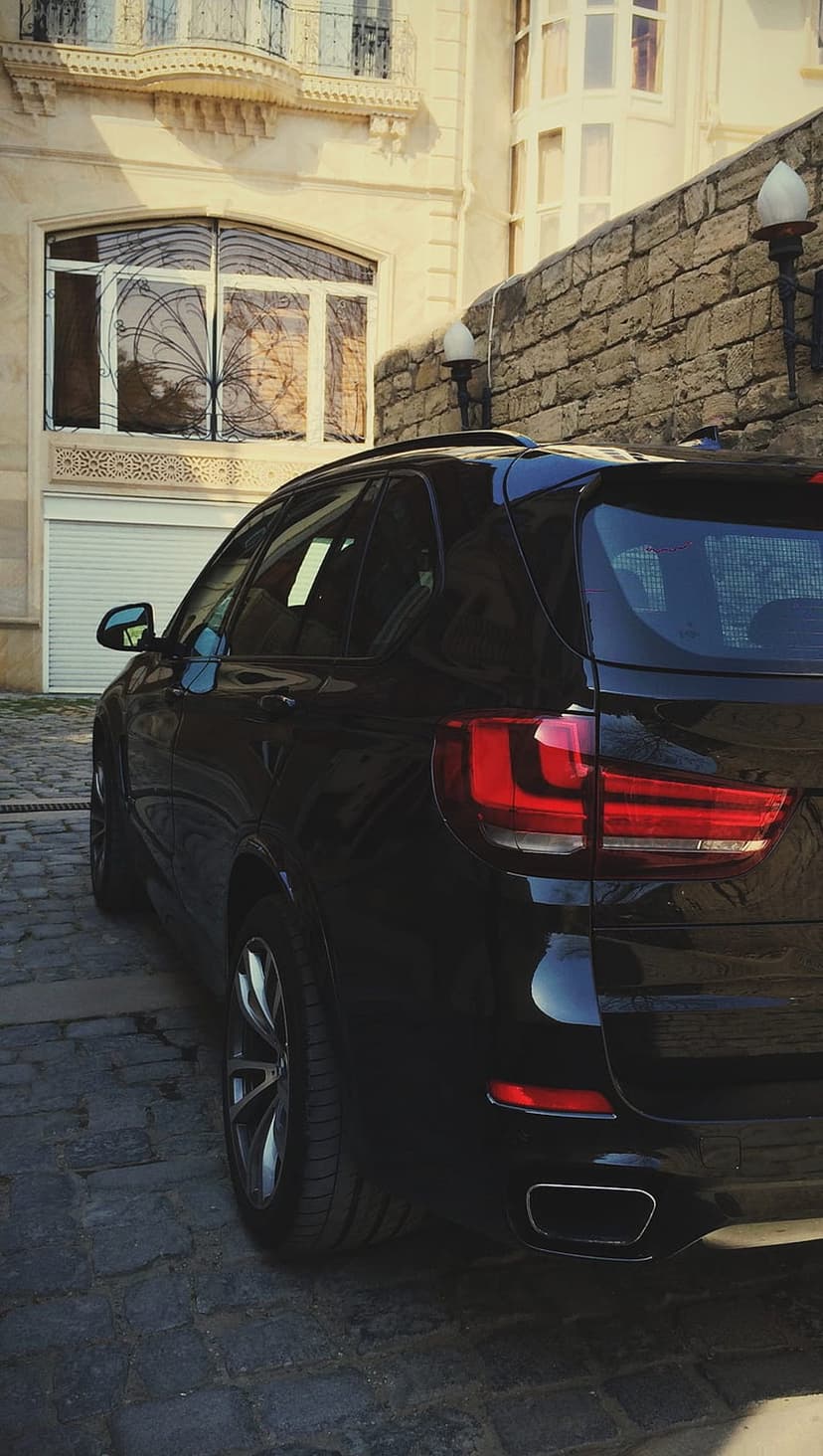 Rear of a black BMW SUV parked on a cobblestone street with a historic stone building in the background.
