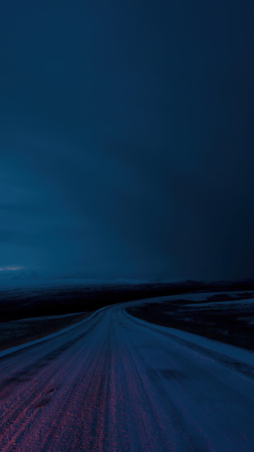Winding road with a pink neon glow crossing a snowy field under a dark indigo sky during winter.