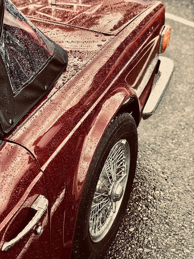 Vintage red convertible with water droplets on the glossy paint and chrome wire wheels against wet asphalt.