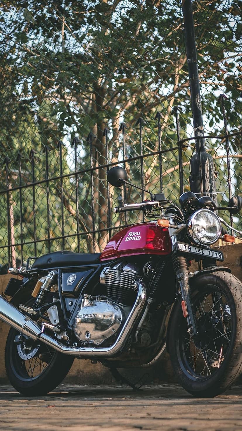 Red Royal Enfield motorcycle with a round headlight and chrome exhaust parked in front of a black metal fence.